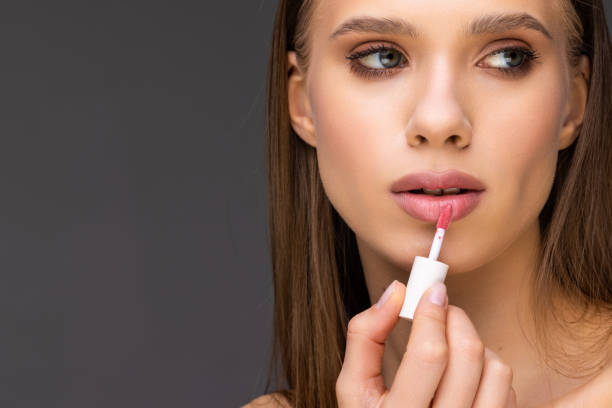istock Young woman make lips with lipstick on gray background 1399707419