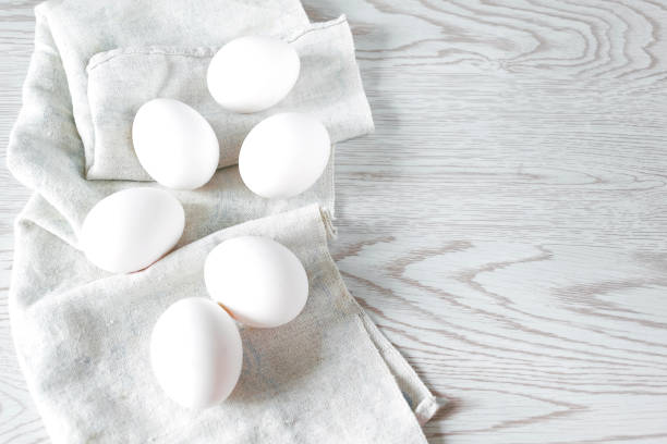 istock White chicken eggs in napkin on white wooden background. Easter composition, mockup. Top view 1399707640