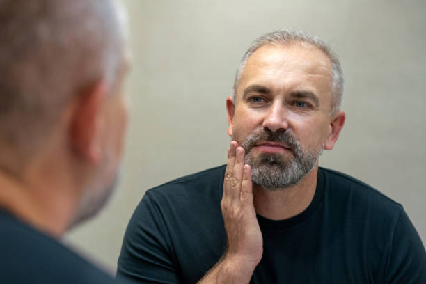 istock Middle-aged handsome man looking in mirror in bathroom touching his beard thinking of cutting it off 1399709044