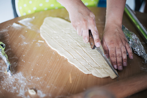 The woman kneads the dough on a table in the kitchen. Kitchen table with food. Woman cutting dough in ribbons and preparing for overflow and baking.