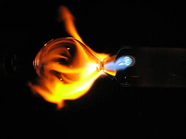 A close up shot of a flame as it contacts a glass bubble, in the creation of an oil lamp. Just visible is the outline of the glass bulb, and the tip of the torch where the flame is coming from. 