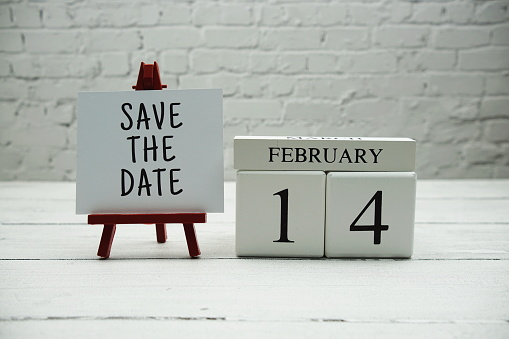 14 February Save the Date text on white brick wall and wooden background