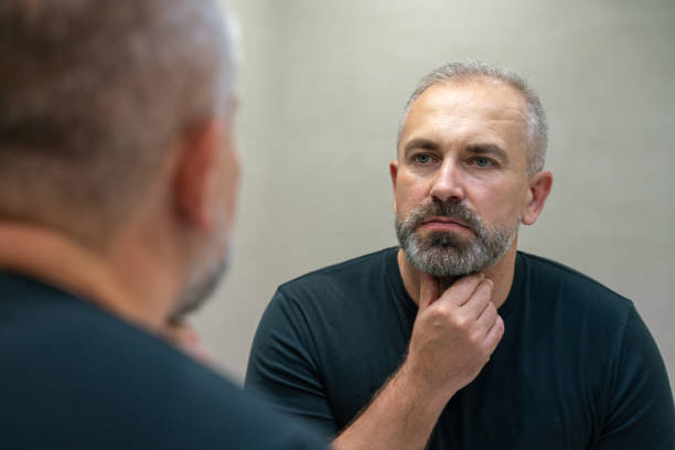 istock Middle-aged handsome man looking in mirror in bathroom touching his beard thinking of cutting it off 1399711636