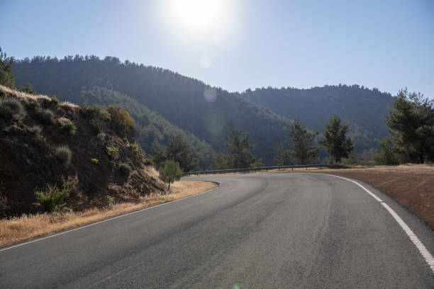 istock Angled road turning left along remote hillside through steep volcanic terrain with forested mountains and sun ahead 1399716007