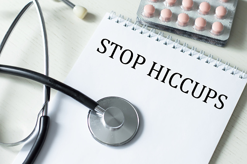 STOP HICCUPS on a notebook on a table next to a stethoscope and tablets
