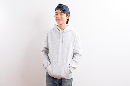 A portrait of a asian young boy with hoodie and cap on white background.