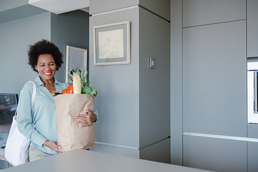 African-American woman holds bag full of groceries at home