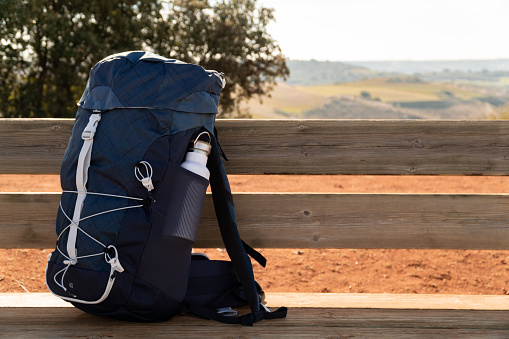 Hiking backpack with a bottle on a wooden bench in the countryside with a background of mountains - sport and health concept