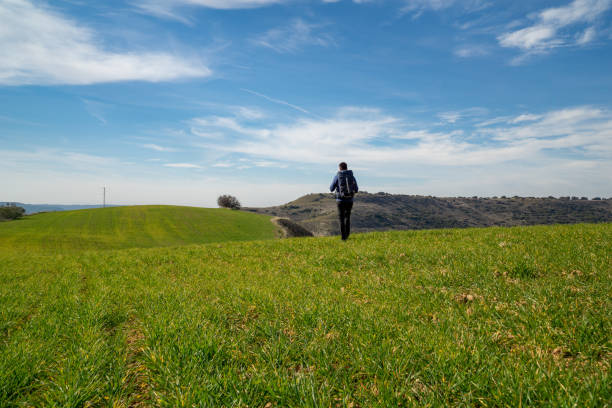 istock Unrecognizable young man walking with a hiking backpack through a green meadow in the middle of nature 1399726093