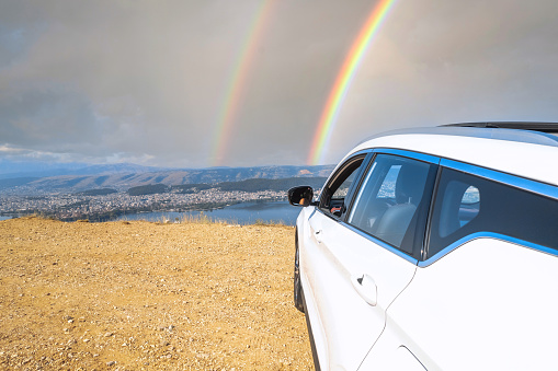 White car stopping on the top of mountain in sunny rainy cloudy day with rainbow.