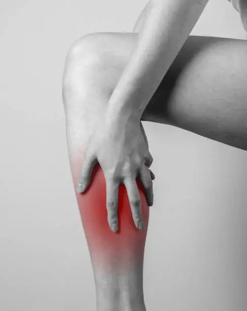 Shin pain. Woman holding leg with red spot. Tendons, muscles inflammation, injury, bone bruise consequences. Black and white. High quality photo