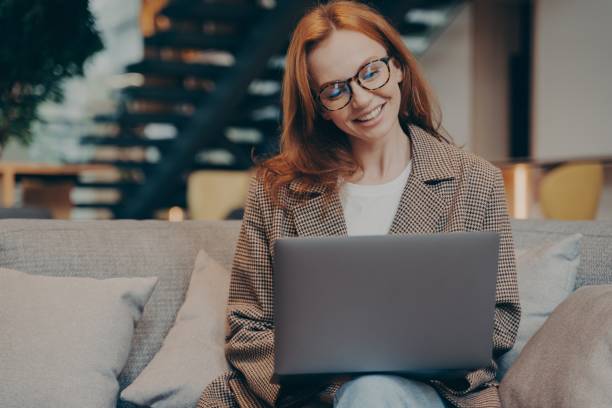 istock Happy female office worker chatting on laptop while sitting on grey couch at office 1399733396