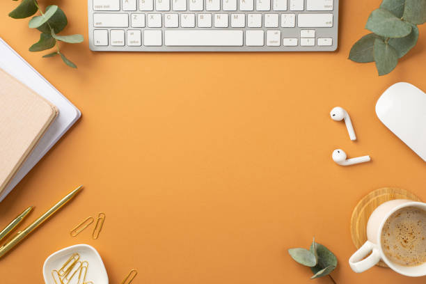 istock Business concept. Top view photo of workplace white keyboard computer mouse notepads wireless earbuds gold pen clips cup of coffee and eucalyptus leaves on isolated orange background with empty space 1399734334