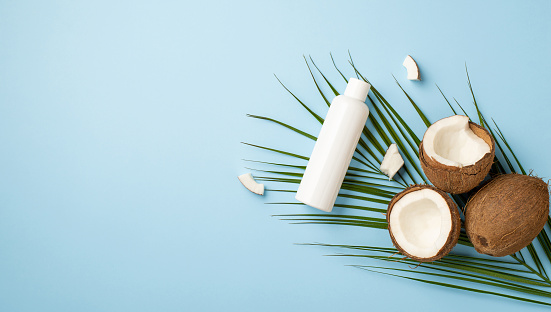 Summer concept. Top panoramic view photo of white sunscreen bottle coconuts and palm leaves on isolated pastel blue background with copyspace