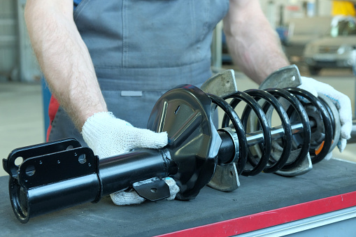 An auto mechanic prepares a new shock absorber rack for installation during repair and maintenance of the car.