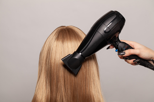 Long smooth shiny healthy hair and hair dryer on gray studio wall background