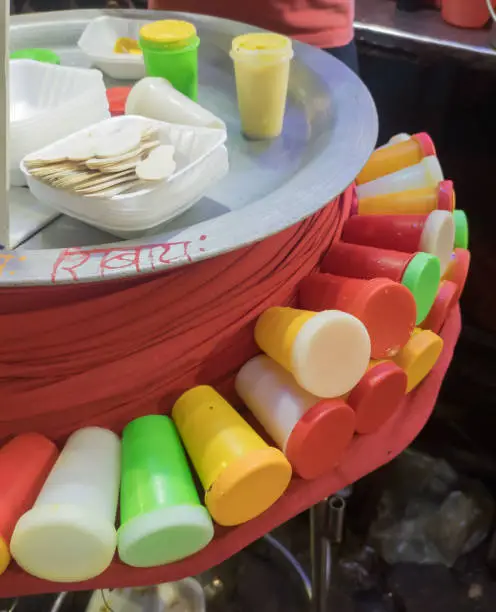 kulfi is a frozen dairy dessert being sold in a market of india. colorful containers of the kulfi kept outside the main pot.this dessert originated in the Indian subcontinent