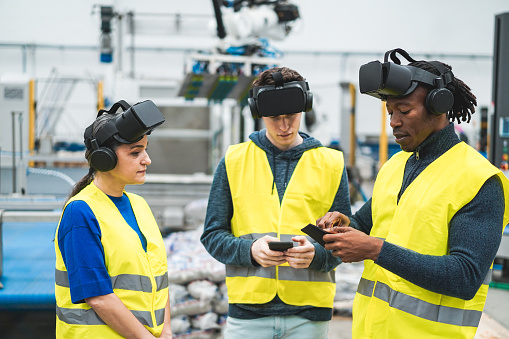 Multiethnic engineers using virtual reality headset inside robotic factory - Industrial and technology concept - Soft focus on african man top hand