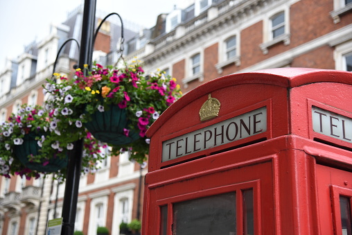 Symbol of London, red telephone booth. Flowers add color to the background of brick buildings.