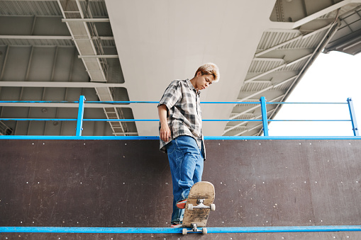 Full length portrait of teenage skater standing on ramp at skatepark and doing tricks, copy space