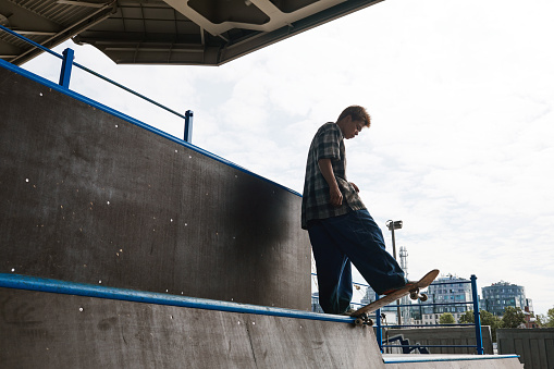 Side view portrait of young skater standing on ramp at skatepark and doing tricks backlit against sky, copy space