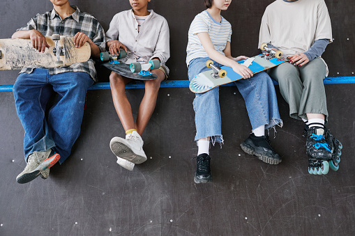Diverse group of teenagers sitting on ramp in skateboarding park low section of feet dangling, copy space