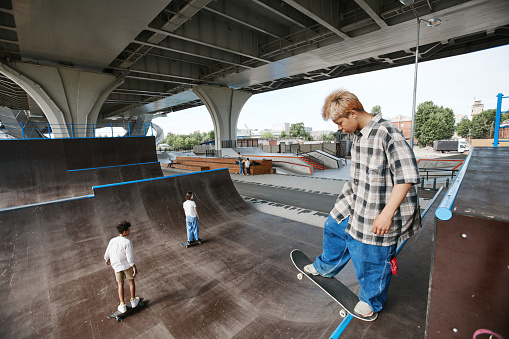 High angle portrait of teenage boy standing on ramp at skatepark and doing skateboarding tricks, copy space