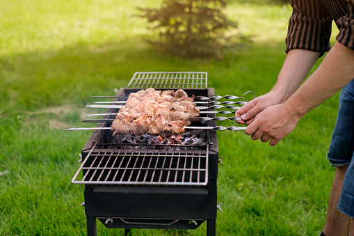 A man is frying a meat kebab in the garden in nature. A weekend in the fresh air. Grill for frying on hot coals