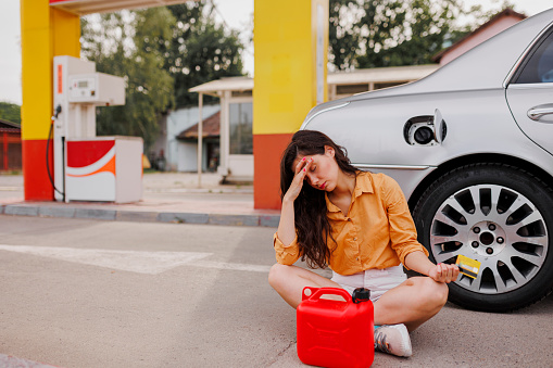 Depressed shocked woman with gas can on gas pump