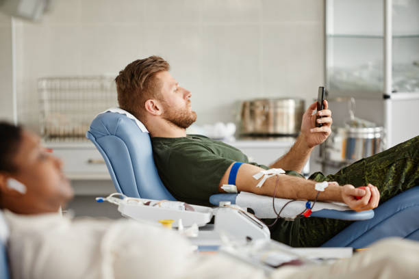 homme utilisant un smartphone dans la vue latérale du centre de don de sang - human blood cell photos et images de collection