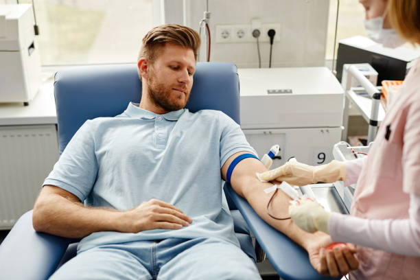 Young Man Donating Blood Portrait of handsome young man preparing for blood donation at med center with nurse helping blood test stock pictures, royalty-free photos & images