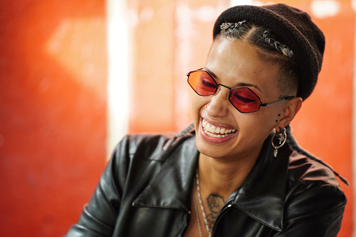 Authentic smiling young beautiful girl in fashionable clothes. Hipster style. Woman in sunglasses, black cap and leather jacket. Real people emotions.