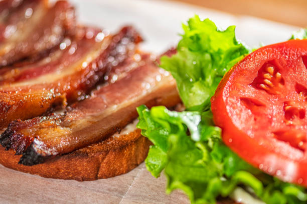 blick hinunter auf die herstellung eines blt-sandwiches, das auf wachspapier und einem schneidebrett sitzt - sandwich bacon lettuce and tomato delicatessen bacon stock-fotos und bilder