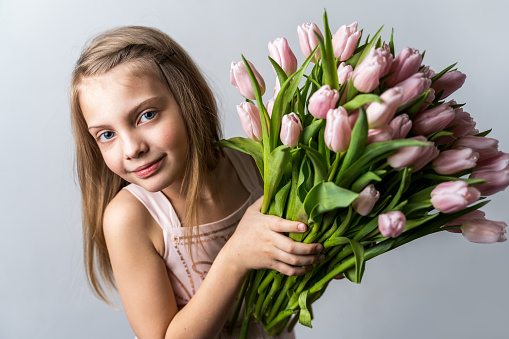 Little beautiful happy girl holding bunch of pink, green tulips in hands. Bouquet, congratulations to the holiday of mother, valentine's. International Women's Day, 8 March.Spring,summer time concept.