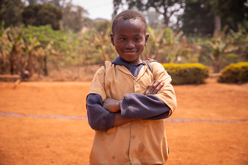 portrait of a young African child with Down syndrome, he has his arms crossed and looks at the camera