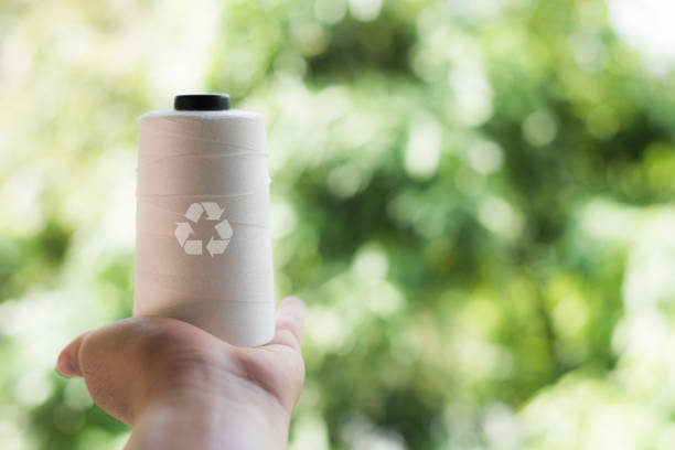 istock Hand holding Raw White Polyester FDY Yarn spool, Polyester Filament Yarn spool.PET fiber Yarn,spun polyester sewing thread with blurred green background. Recycle icon, sustainable icon and Bottle icon 1399760412