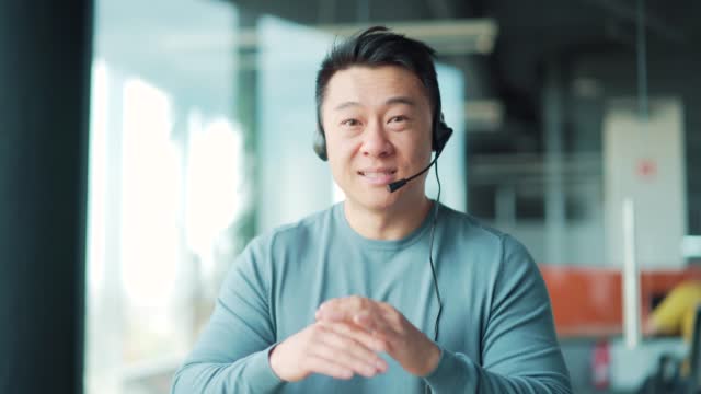 Portrait asian man talking video call with headset looking at camera. Webcam view. Male Freelance Teacher Lecturer Talk Online Support Meeting or Conference.
