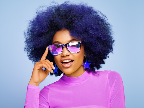 Beauty portrait of African American girl in colored holographic sunglasses. Beautiful black woman on blue background. Cosmetics, makeup and fashion