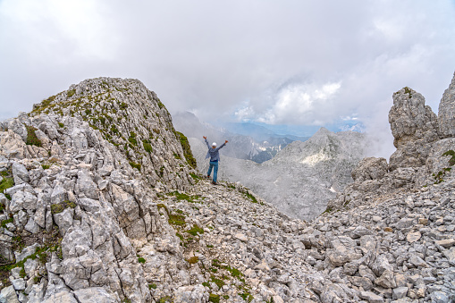 Rear view of one woman standing with arms raised on top of mountain peak in highlands of Triglav national park, Julian Alps