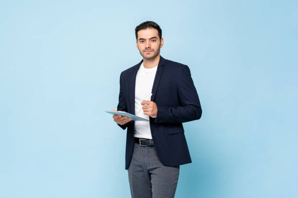 умный красавец кавказец в полуформальном деловом костюме держит планшетный компьютер с ручкой в светло-синем цвете изолированного студий� - pen business person men standing стоковые фото и изображения