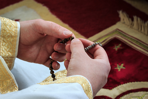 Religious muslim man praying with prayer-beads (tesbih) in hands on red prayer rug.