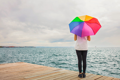 Colorful umbrella in the hands of woman standing on a pier