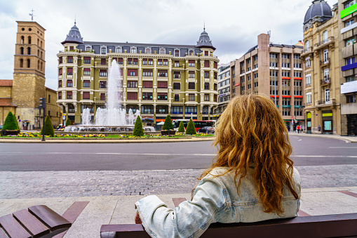 Woman sitting on a bench contemplating the buildings of the city of Leon, Spain