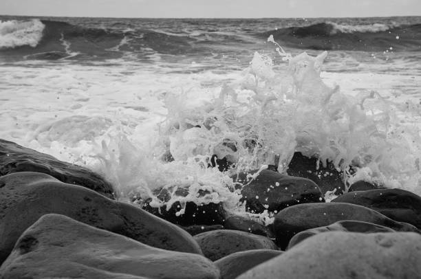 Turquoise wave breaking on a beach in sea with silver clouds