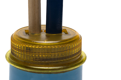 Close-up of plastic barrel sharpener with two shafts in which a thin pencil and a thick crayon are stuck on white background