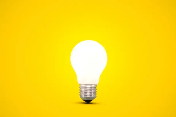 Photo of Glowing light bulb isolated on a bright yellow background.