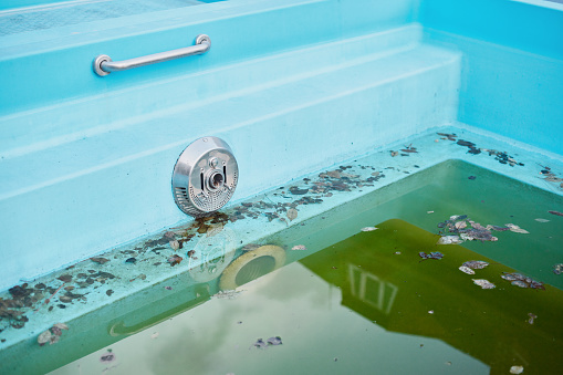 Close-up of an outdoor swimming pool with dirty water in spring.