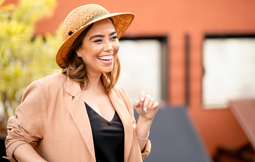 Young woman wearing a sun hat laughing while sitting outside on a rooftop terrace in the summertime