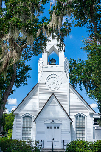 Classic white church resting under a clear blue sky with a bell in its beautiful steeple, surrounded by old southern oak trees dripping with Spanish moss in Kissimmee, Florida