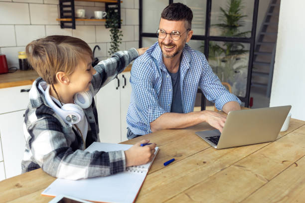 istock Father helping his teenage son with homework while working from home in the kitchen. Concept of parenthood, fatherhood, spending quality time together. Using technology, gadgets, devices for learning 1399783710